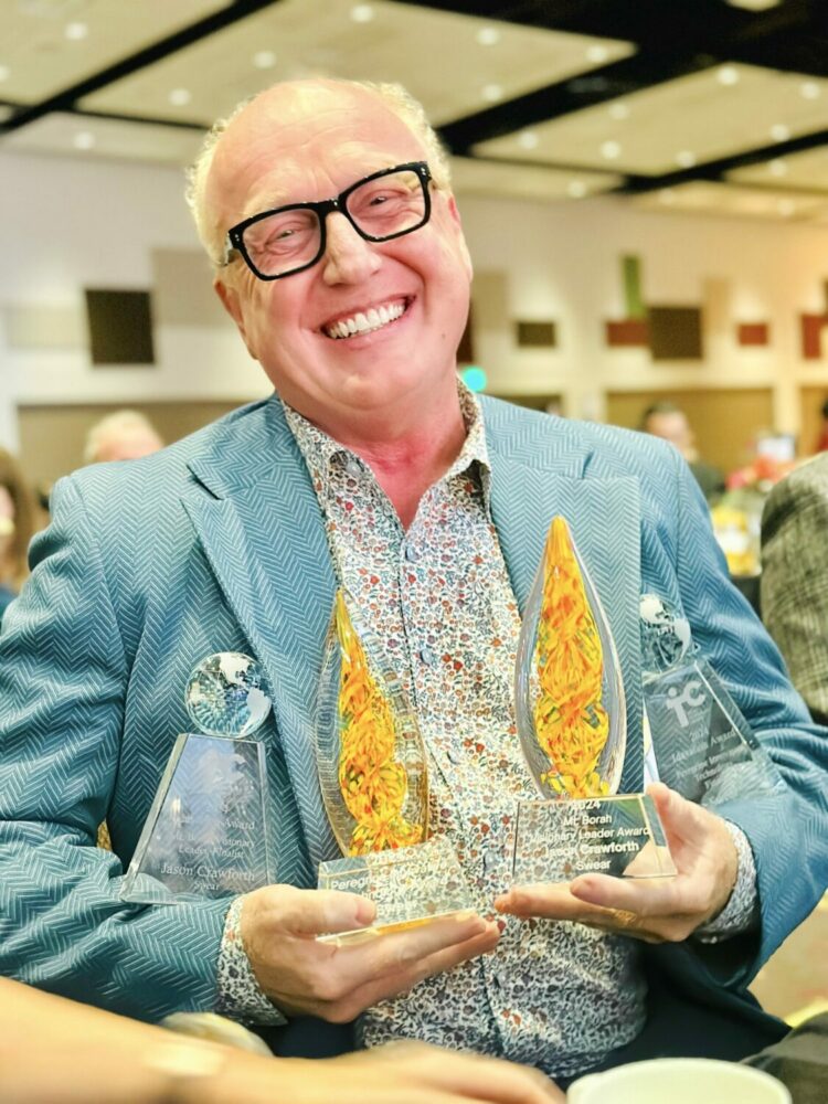 SWEAR CEO Jason Crawforth smiling while holding multiple awards, including the Peregrine Innovation Award and Mt. Borah Visionary Leader Award, at a formal event.